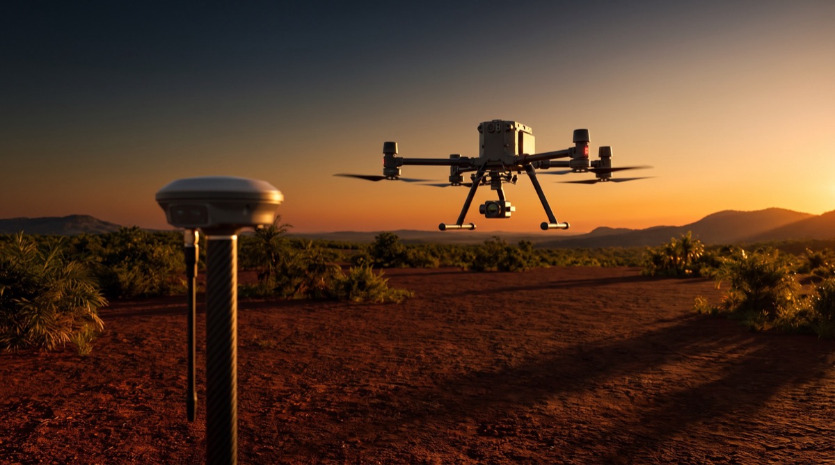 Receptor RTK em primeiro plano e drone de levantamento sobrevoando terreno ao entardecer